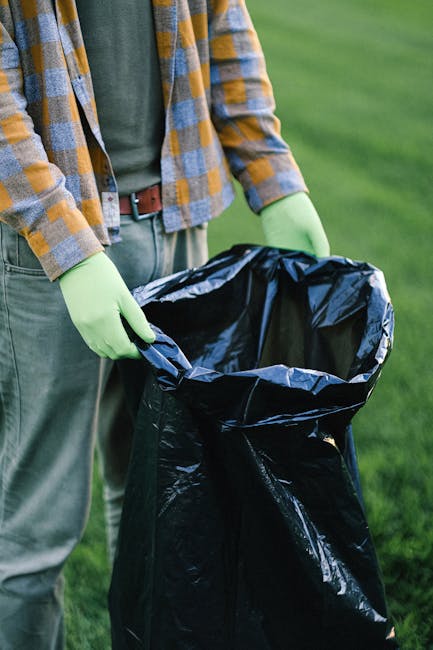 Five large wheeled rubbish bins are positioned in a straight line against a plain white wall. The bins are made of dark grey plastic with a textured surface and are equipped with yellow lids that cont